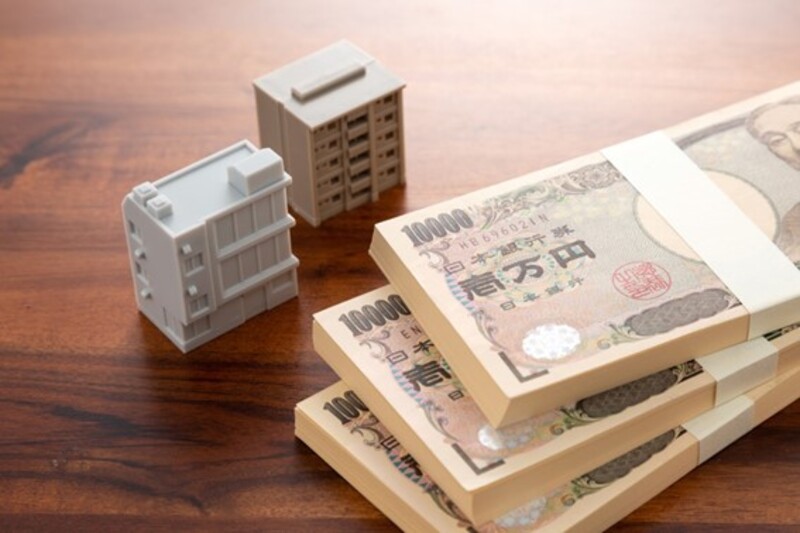 小さなマンションの模型2つと100万円札束3つ
