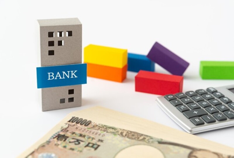 銀行の模型と現金と電卓とカラフルな直方体ブロック