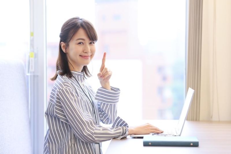 パソコンの前でナンバーワンポーズをする女性