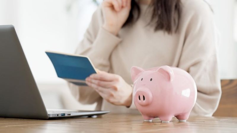 通帳を見ている女性とブタの貯金箱
