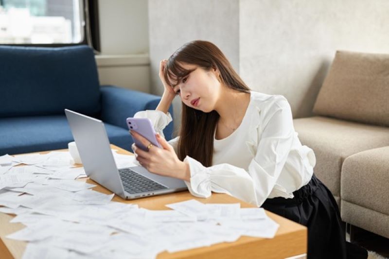 スマホ画面を見ながら頭を抱える女性