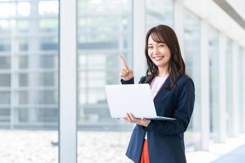 パソコンを持ってナンバーワンポーズをする女性
