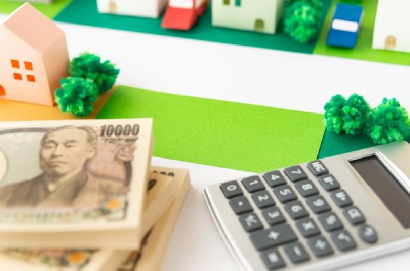 模型の住宅街に置かれた一万円札束と電卓