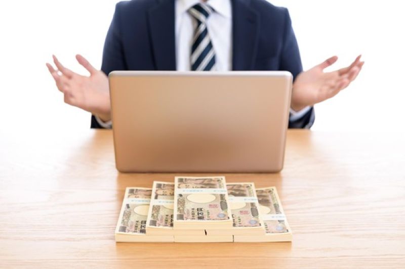 パソコンの前で両手を広げる男性と一万円札束