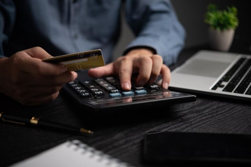 クレジットカードを持ち電卓を使用する男性